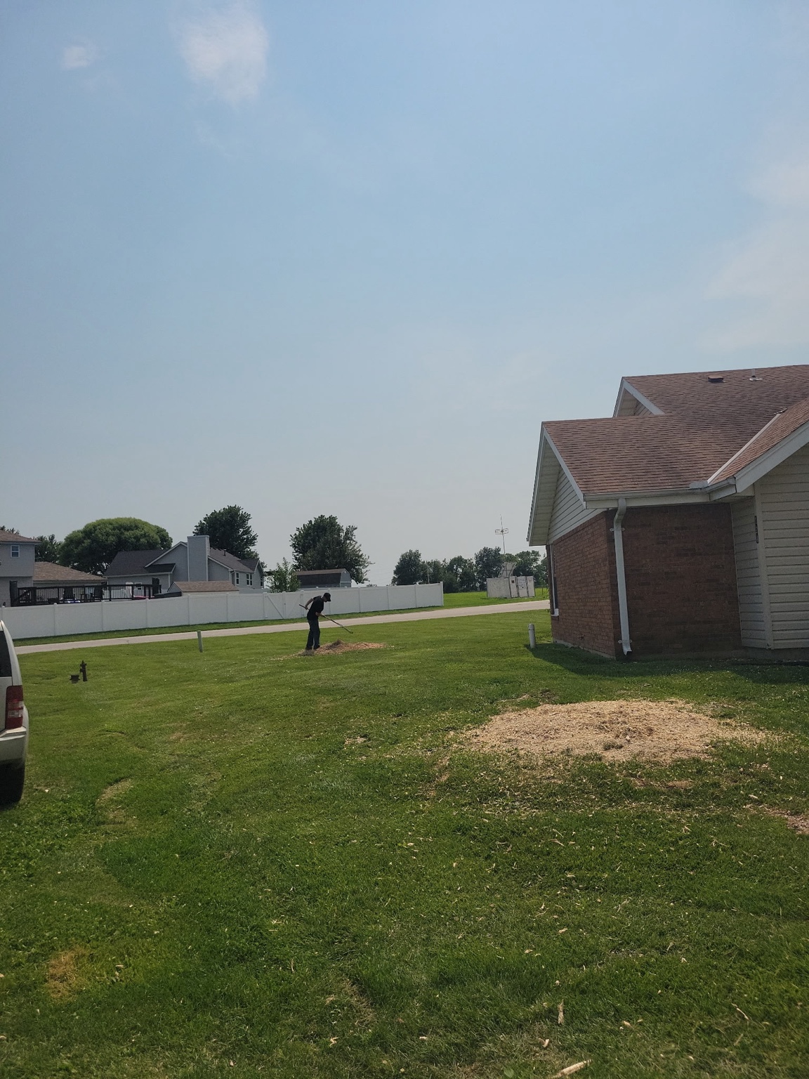 Crew member raking stump grindings off a clean lawn after tree work at a Warrensburg, MO home